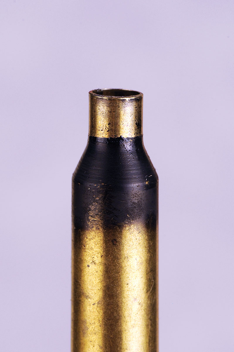 A close-up shows how the neck-sizing die works on a fired case. Smoking the neck and shoulder helps to monitor the progress of the die downward on the case.